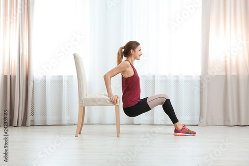 Fototapeta Naklejka Na Ścianę i Meble -  Young woman exercising with chair indoors. Home fitness