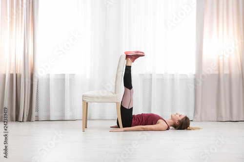 Young woman exercising with chair indoors. Home fitness