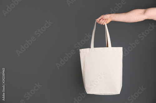 Man holding cotton shopping eco bag on grey background. Mockup for design