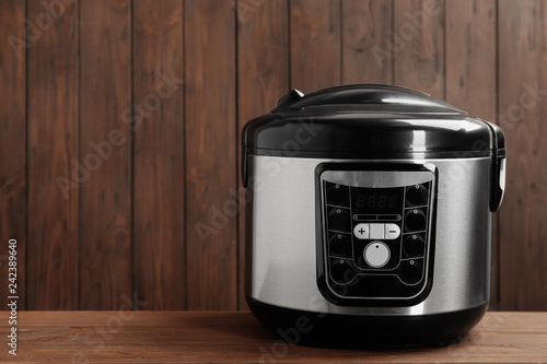 Modern powerful multi cooker on table against wooden background. Space for text