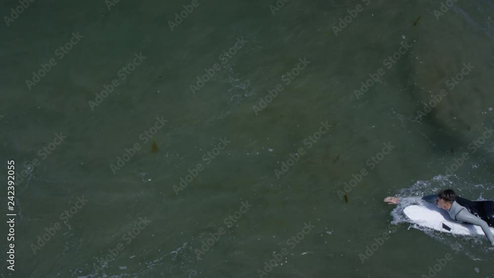 Aerial View Of Surfer Paddling Out To Sea On His Board, He Swims Right To Left Across Frame, Slow Motion Aerial View Of Surfer Paddling Out To Sea On His Board, He Swims Right To Left Across Frame, Slow Motion