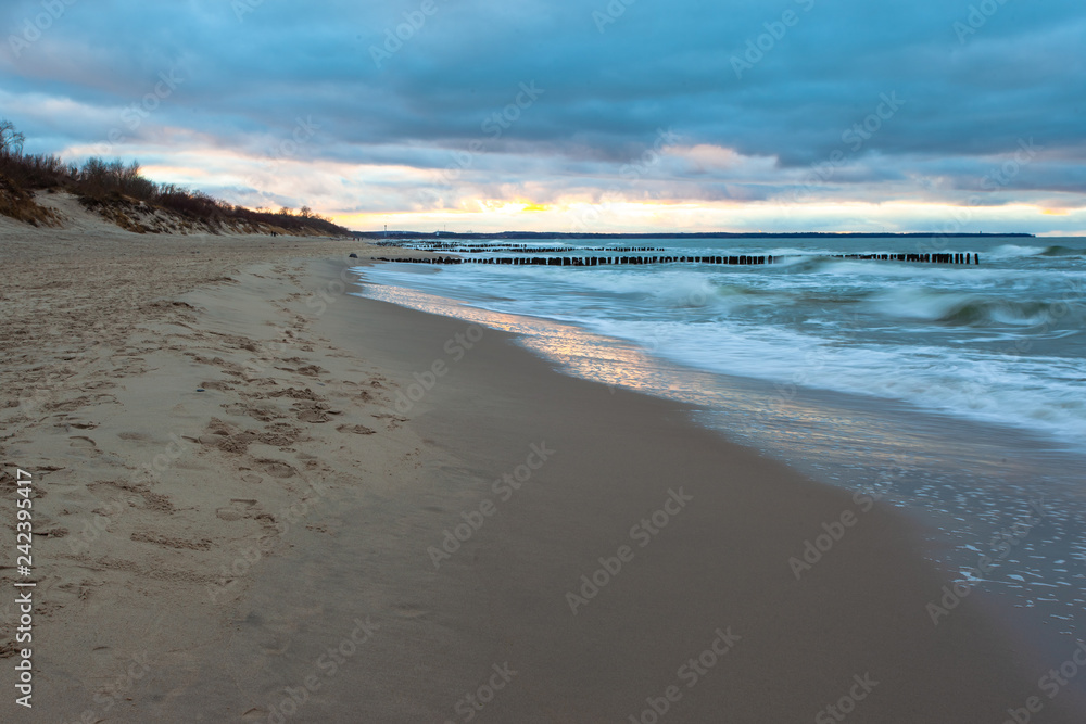 wide sandy beach with a breakwater by the cold sea in cloudy weather on long exposure