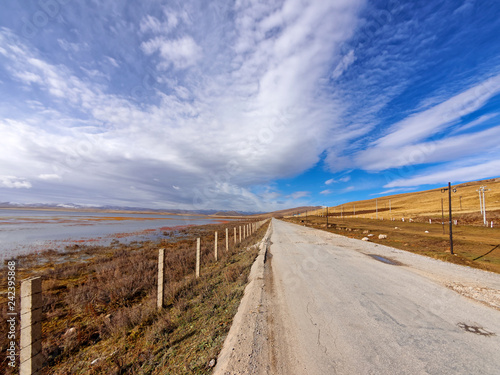 Straight country road among mountains and lake with beautiful cloudy sky background in gahai National Nature Reserve park, amazing landscape in Gannan, Gansu province, China.