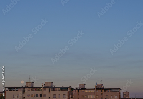 full moon setting over residential buildings in the morning after sunrise. minimalist composition with copy space