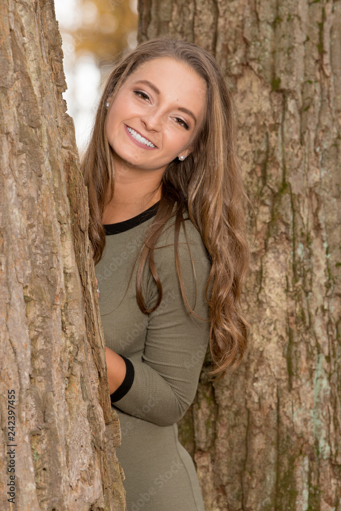 Beautiful young woman in stunning green dress and poses in the autumn woods - fall fashion - standing next to large tree Beautiful young woman in stunning green dress and poses in the autumn woods - fall fashion - standing next to large tree