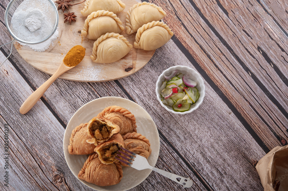 Traditional curry puffs stuffed chicken with raw curry puffs on wooden table as background Traditional curry puffs stuffed chicken with raw curry puffs on wooden table as background