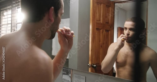 Young homosexual hispanic people and male beauty. Beautiful latino person grooming in bathroom in hotel room for morning routine, body care. White gay metrosexual man brushing teeth in front of mirror