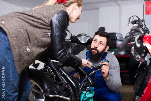 Smiling male worker assisting female customer in repairing motorcycle in workshop