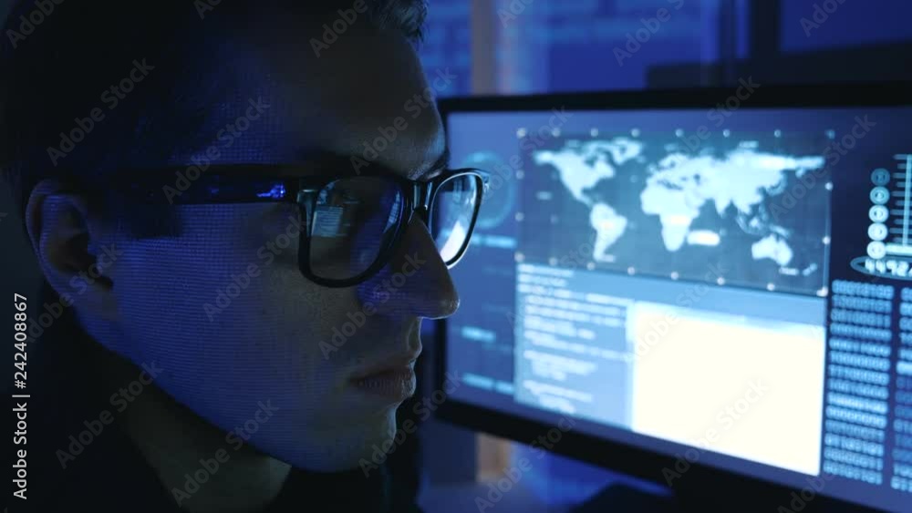 Close-up portrait of a Man Professional Geek Programmer in glasses working at computer in a data center filled with monitor screens Close-up portrait of a Man Professional Geek Programmer in glasses working at computer in a data center filled with monitor screens