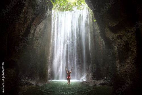Fotobehang Woman with arms raised to gorgeous scenic epic majestic waterfall in cave with l