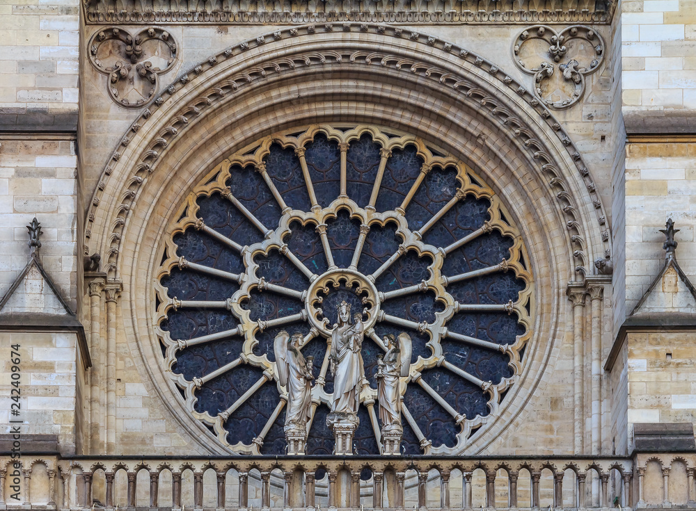Closeup of the Notre Dame de Paris Cathedral facade with the oldest rose window installed in 1225 which forms a halo above the Virgin with Child statue placed in front of it