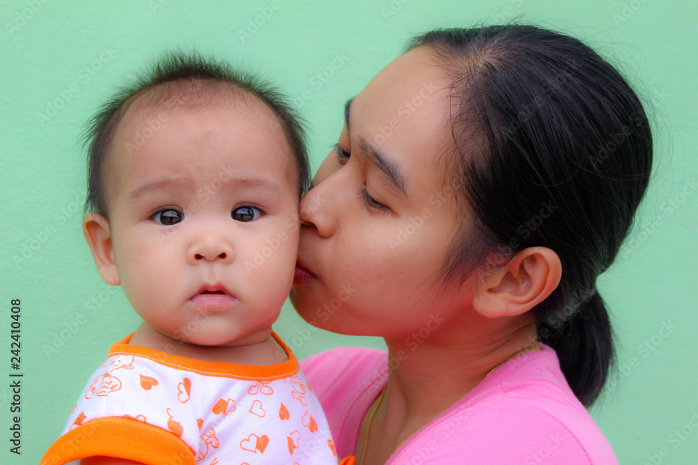Asian mother kiss to baby's cheek on green background. Asian mother kiss to baby's cheek on green background.