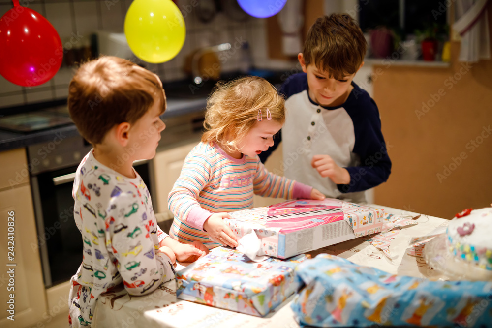 Fototapeta premium Adorable little toddler girl celebrating second birthday. Baby child and two kids boys unpacking gifts. Happy healthy children siblings is suprised about big boxes and toys