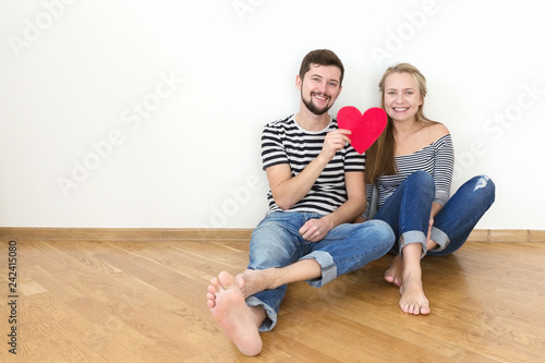 A couple in love sitting on the floor with a red heart in hand.