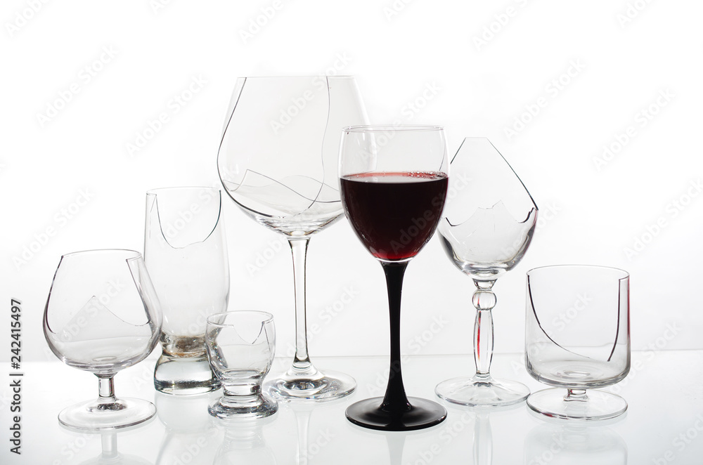 A glass of red wine on the background of broken glasses on a light background A glass of red wine on the background of broken glasses on a light background