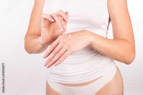 Female hands with french manicure applying hand cream, white background, closeup, front view