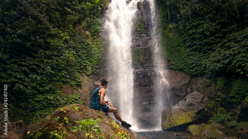 man sitting on a stone overlooking the waterfall Bali Indonesia