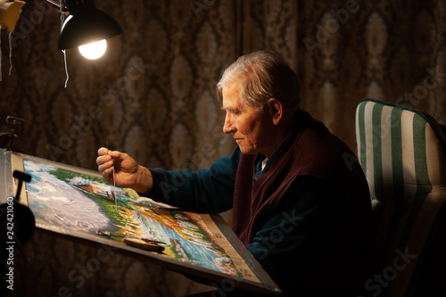 Elderly man woving a tapestry under bright light in living room on winter evening photo