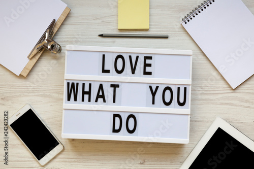 Modern board with text 'Love what you do', tablet, smartphone, notepad and pencil over white wooden background, top view. Business concept. From above, flat-lay, overhead.