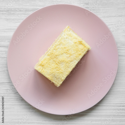 Piece of Napoleon Cake on pink plate over white wooden surface, overhead view. Flat lay, from above.