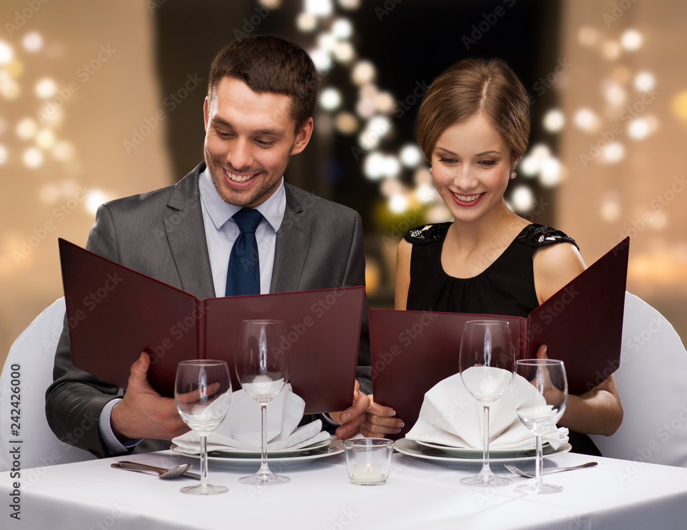 dating, luxury and people concept - happy couple with menus at restaurant over festive lights on background