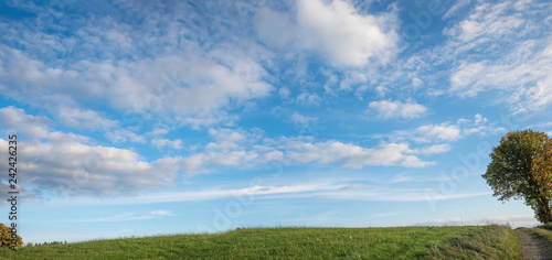 Grüne Hügelkuppe und blauer Himmel mit Wolken