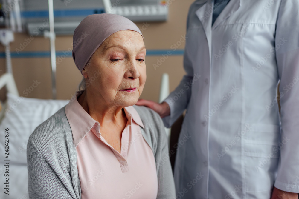 selective focus of doctor consoling senior woman with cancer in hospital