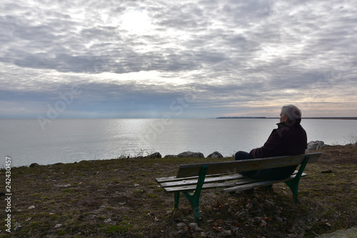 Silhouette of a man over 50 years sitting on an old wooden bench above the see in a cloudy winter day. Senior man quietly watching the see. Nostalgic mood. Duran Kulak, Bulgaria