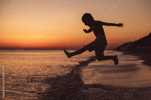 One happy little boy playing on the beach at the sunset time.