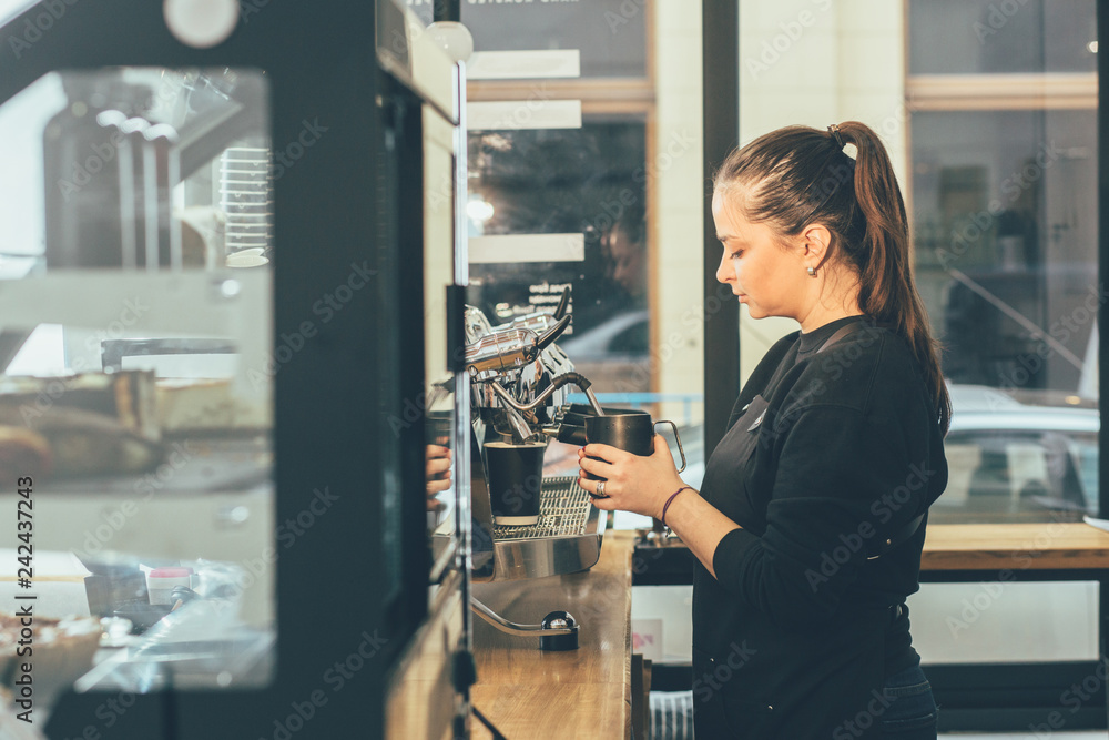 Barista enjoying working process preparing coffee drinks using professional equipment in cafeteria with display showcase on foreground. Skilled waitress on coffee machine making cappuccino. Toned Barista enjoying working process preparing coffee drinks using professional equipment in cafeteria with display showcase on foreground. Skilled waitress on coffee machine making cappuccino. Toned