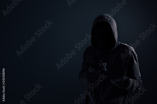 Hooded computer hacker with obscured face using digital tablet
