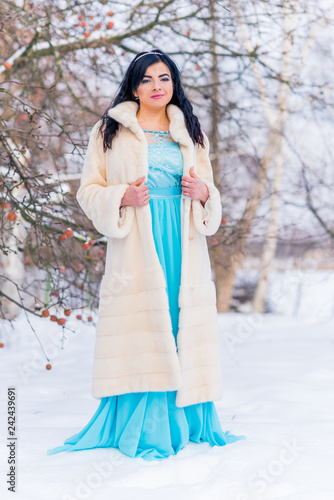 Arabic woman in mink fur coat and blue long romantic dress at snowy day, femininity and grace concept, winter fairytale 