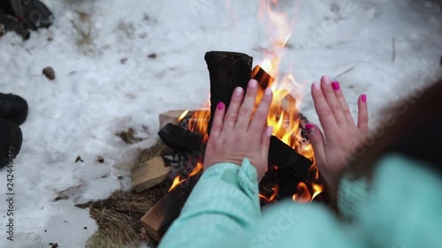 Girl warms her hands over the fire in the forest in winter.