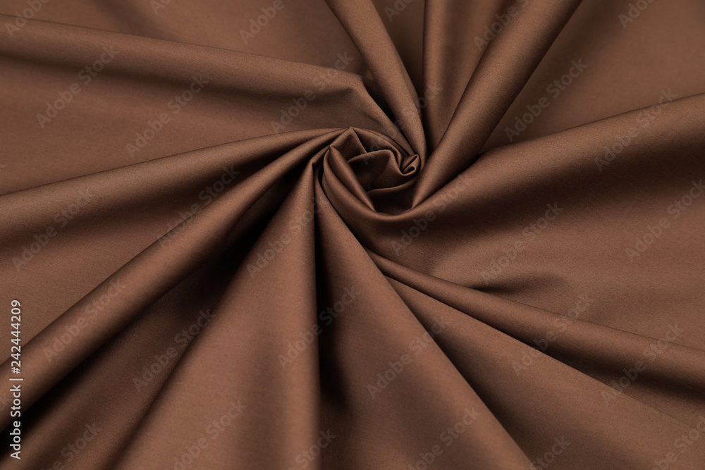 Obraz premium Brown sateen fabric with a shade of bitter chocolate is laid by folds on diagonal to the center in the form of a spiral