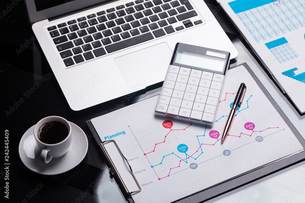 Modern calculator is on the notebook and on the sheet with the schedule next to the coffee Cup Modern calculator is on the notebook and on the sheet with the schedule next to the coffee Cup