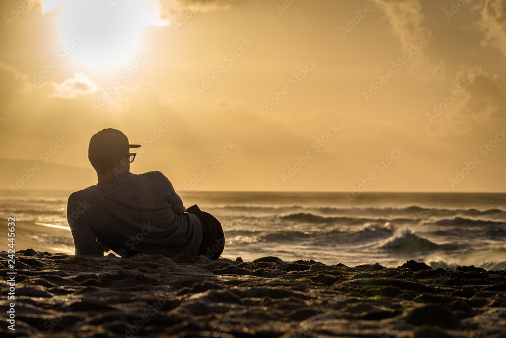 Silhouette of young caucasian male laying on Sunset Beach in Hawaii looking out at sunset over the ocean