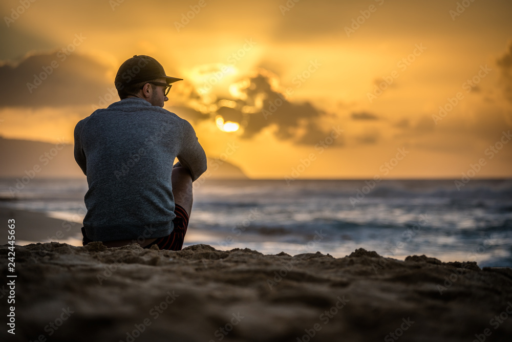 Silhouette of young caucasian male sitting on Sunset Beach in Hawaii looking out at sunset over the ocean