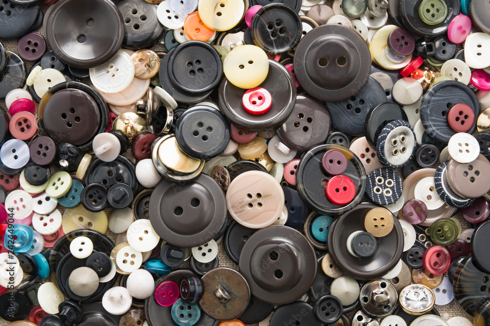 A lot of colorful sewing buttons of different colors of metal and plastic on linen light natural fabric A lot of colorful sewing buttons of different colors of metal and plastic on linen light natural fabric
