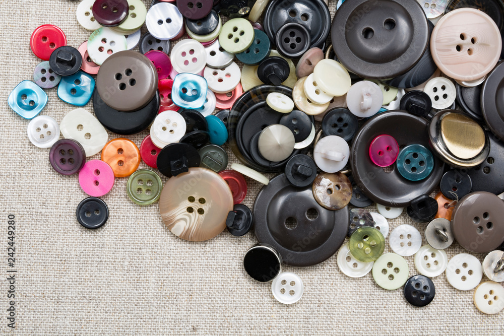A lot of colorful sewing buttons of different colors of metal and plastic on linen light natural fabric A lot of colorful sewing buttons of different colors of metal and plastic on linen light natural fabric