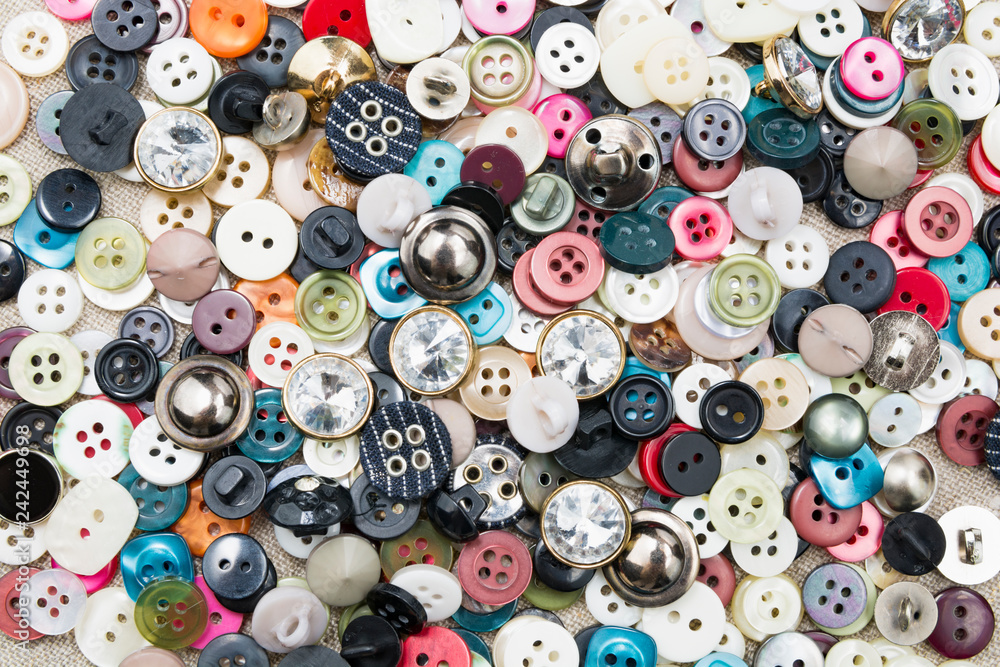 A lot of colorful sewing buttons of different colors of metal and plastic on linen light natural fabric A lot of colorful sewing buttons of different colors of metal and plastic on linen light natural fabric
