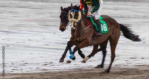 Galloping race horse and jockey competing on wet sand beach, motion blur speed effect