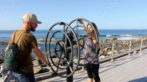 Man and woman doing wrist exercise on spinning wheel machine by the sea in Agaete, Gran Canaria. Young couple practicing workout outdoors in Canary Islands, Spain photo