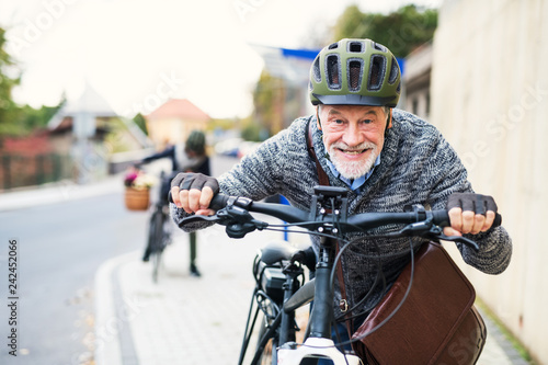 Active senior couple with electrobikes standing outdoors on a road in town.