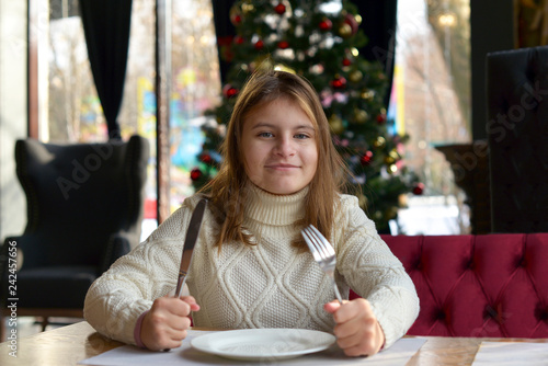 Teen girl sitting at a table in a festive cafe waiting for a delicious dinner on new year's eve.