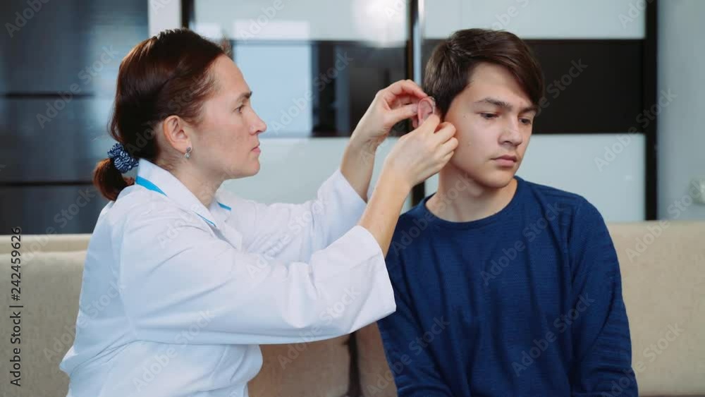Woman doctor puts on hearing aid boy teenager. Woman doctor puts on hearing aid boy teenager.