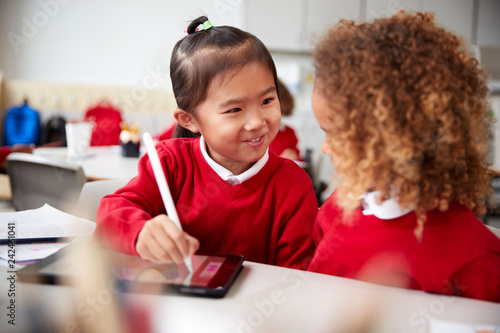 Fotografi Close up of two kindergarten schoolgirls wearing school uniforms, sitting at a d
