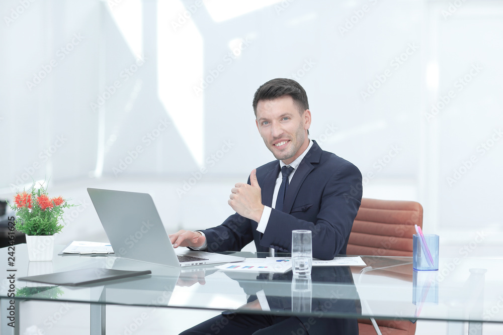 close up.smiling businessman working on laptop and showing thumb up