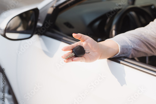 Woman holding the ignition keys of a car in her hand dangling them through the open side window