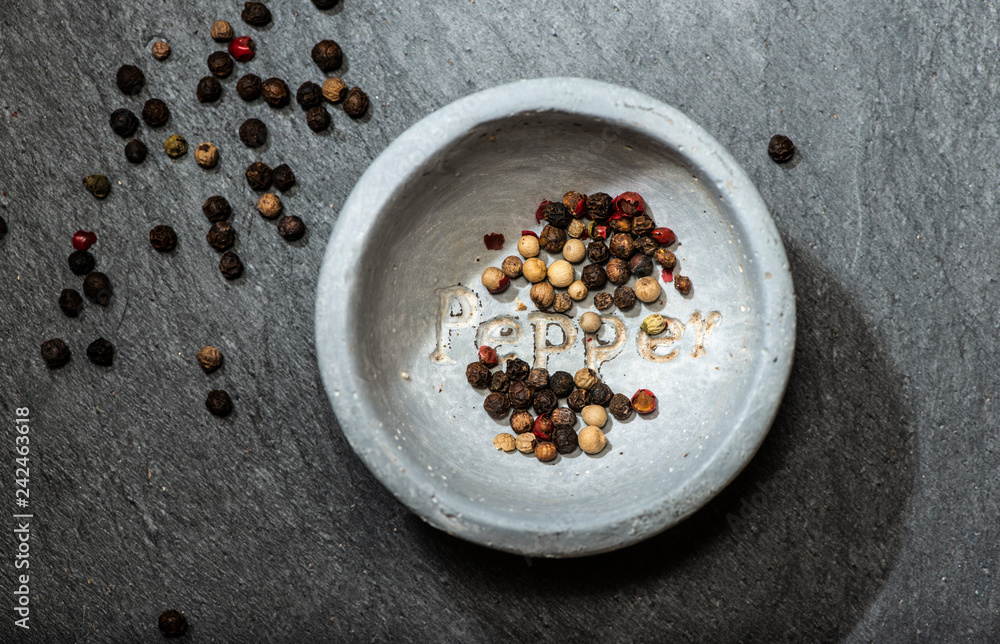 Black pepper in small bowl for spices on dark background. Bowl with text Pepper on the bottom. Black pepper in small bowl for spices on dark background. Bowl with text Pepper on the bottom.