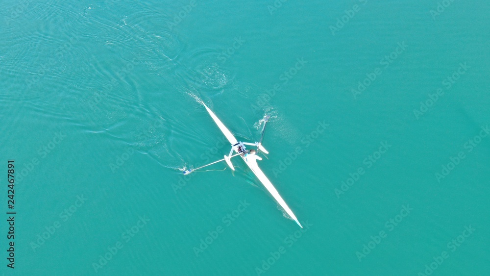 Aerial drone bird's eye view of sport canoe operated by young fit man in turquoise clear waters Aerial drone bird's eye view of sport canoe operated by young fit man in turquoise clear waters